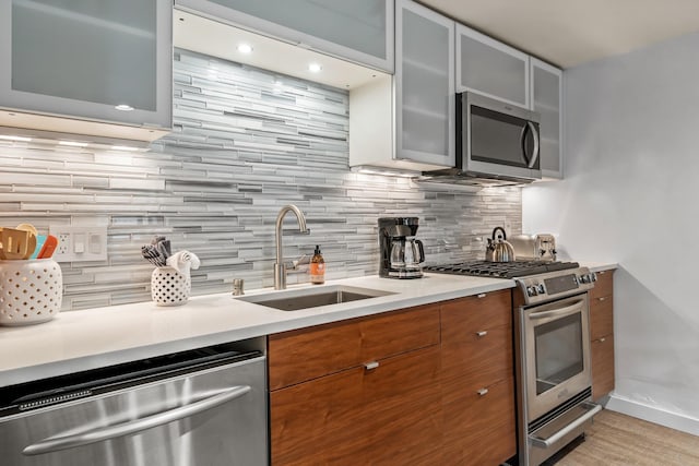 kitchen featuring glass insert cabinets, appliances with stainless steel finishes, brown cabinets, light countertops, and a sink