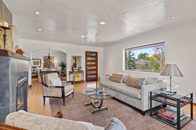 living area featuring light wood-type flooring, arched walkways, a warm lit fireplace, and recessed lighting