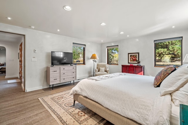 bedroom featuring light wood-type flooring, baseboards, arched walkways, and recessed lighting