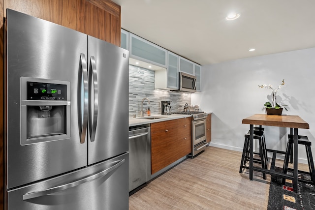 kitchen featuring tasteful backsplash, sink, light wood-type flooring, and appliances with stainless steel finishes