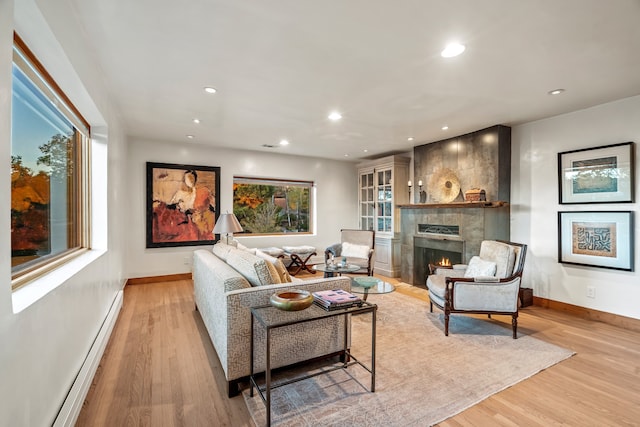 living room featuring a tile fireplace, light hardwood / wood-style floors, and a baseboard heating unit