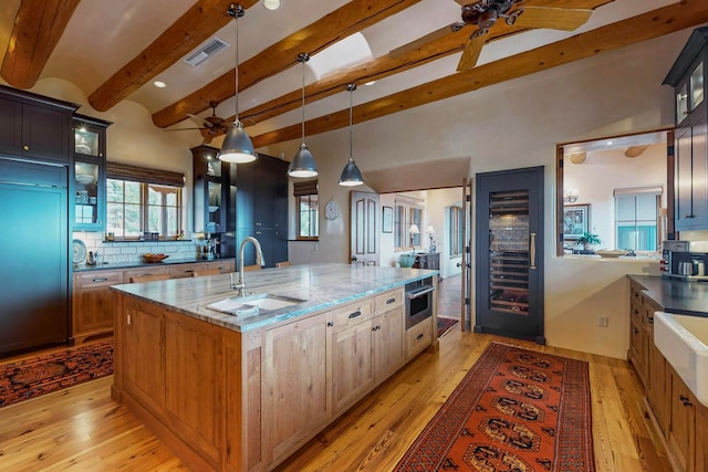 kitchen with light stone counters, a kitchen island with sink, hanging light fixtures, and light hardwood / wood-style flooring