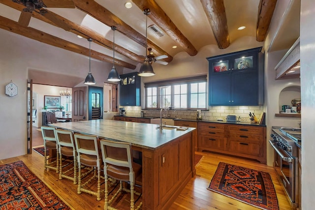 kitchen featuring sink, high end stove, an island with sink, light hardwood / wood-style floors, and decorative light fixtures