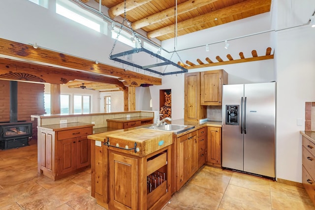 kitchen with beam ceiling, a wood stove, sink, kitchen peninsula, and stainless steel fridge