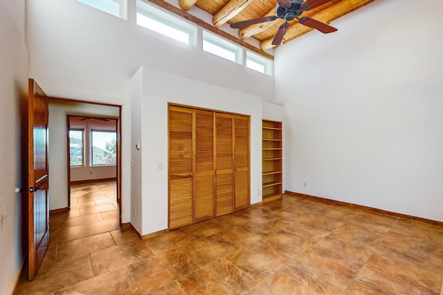 unfurnished bedroom with a towering ceiling, wood ceiling, ceiling fan, beam ceiling, and a closet