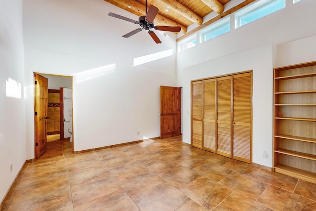 unfurnished bedroom featuring a towering ceiling, ceiling fan, beam ceiling, wooden ceiling, and multiple closets