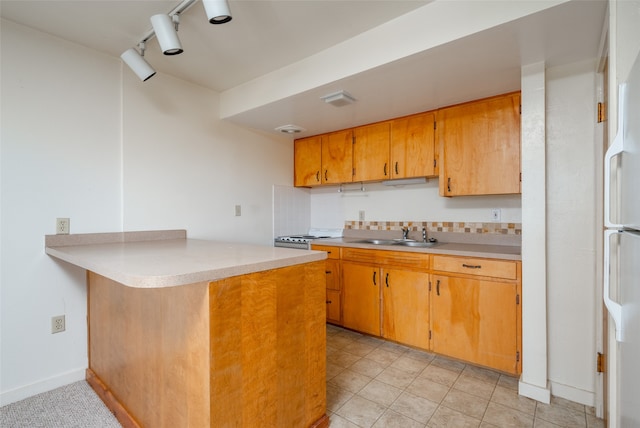 kitchen featuring stove, rail lighting, decorative backsplash, sink, and kitchen peninsula