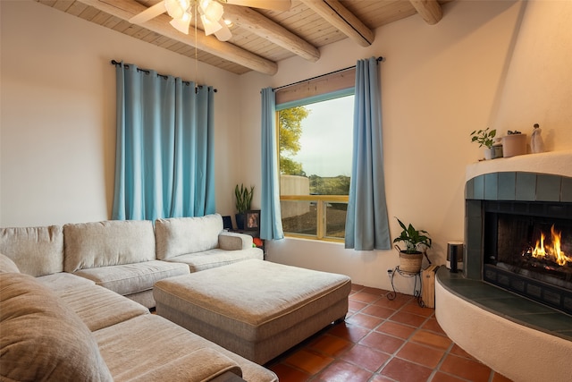 living room featuring ceiling fan, wooden ceiling, dark tile patterned floors, beamed ceiling, and a tiled fireplace