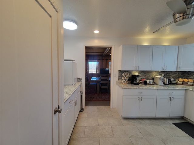 kitchen with white cabinets, decorative backsplash, and light stone countertops