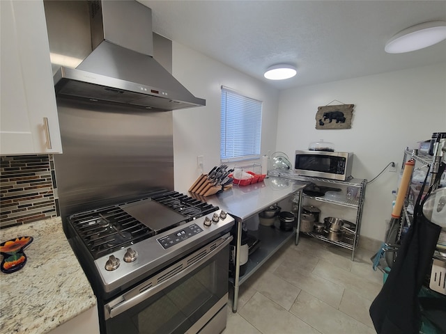 kitchen with light stone countertops, wall chimney exhaust hood, tasteful backsplash, white cabinets, and appliances with stainless steel finishes