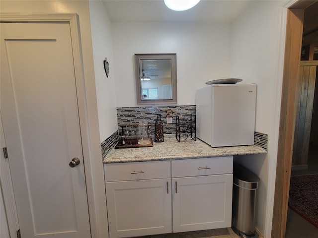 bar with decorative backsplash, white refrigerator, white cabinetry, and light stone counters