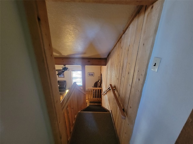 interior space featuring ceiling fan, wood walls, lofted ceiling, and a textured ceiling