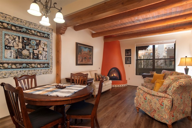 dining room featuring wooden ceiling, dark wood-type flooring, beamed ceiling, a notable chandelier, and a large fireplace