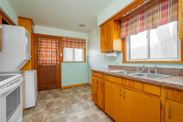 kitchen featuring electric range, stacked washer and dryer, a healthy amount of sunlight, and sink