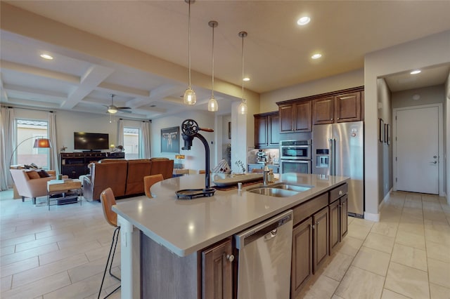 kitchen with coffered ceiling, a center island with sink, sink, decorative light fixtures, and stainless steel appliances