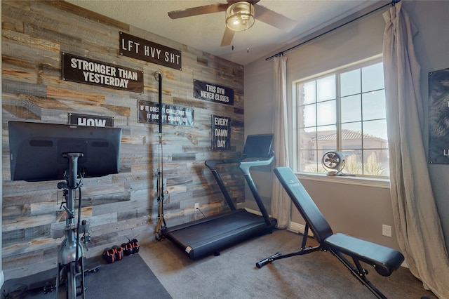 exercise area with carpet flooring, ceiling fan, and wood walls