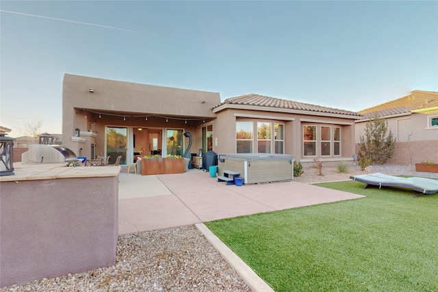 back of house with a lawn, a patio area, and a hot tub