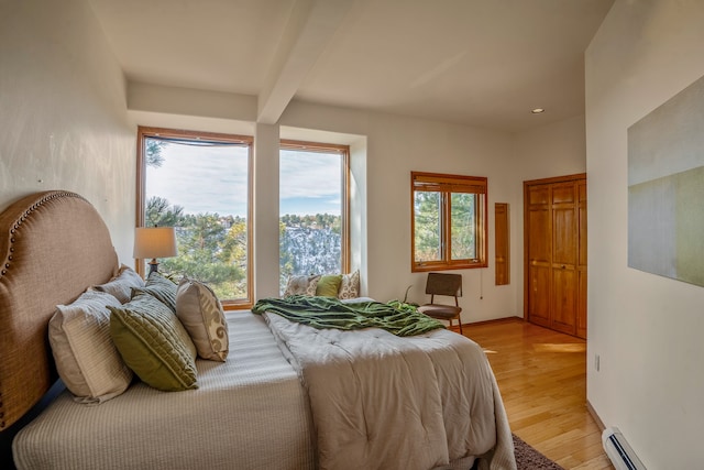 bedroom with beam ceiling, multiple windows, light hardwood / wood-style floors, and a baseboard heating unit