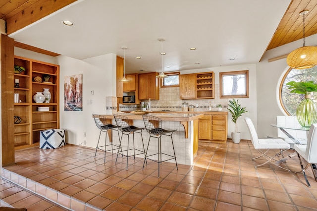 kitchen with kitchen peninsula, a kitchen bar, tasteful backsplash, wood ceiling, and pendant lighting