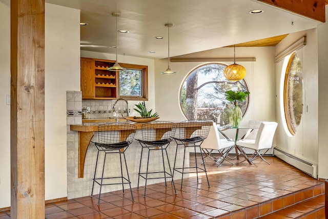 bar with backsplash, a baseboard heating unit, sink, pendant lighting, and dark tile patterned flooring