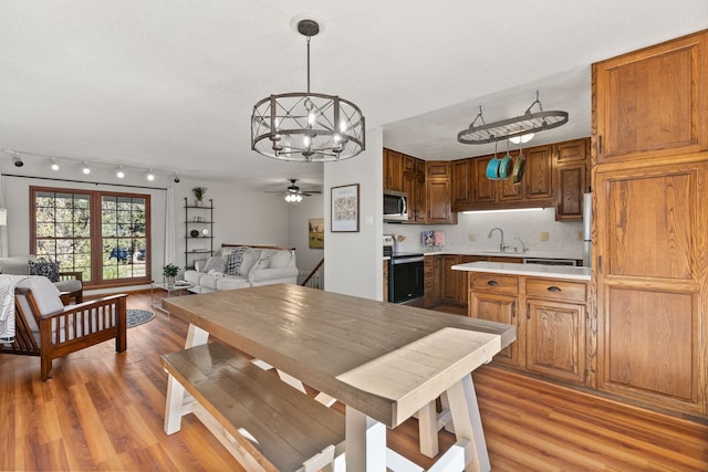 kitchen featuring tasteful backsplash, ceiling fan with notable chandelier, stainless steel appliances, wood-type flooring, and hanging light fixtures