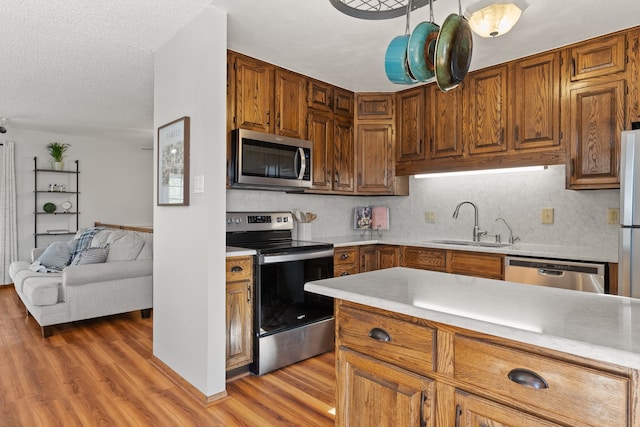 kitchen featuring backsplash, a textured ceiling, stainless steel appliances, sink, and light hardwood / wood-style flooring