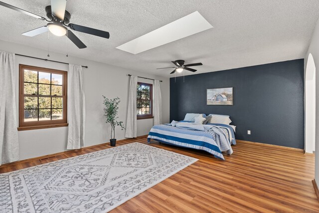 bedroom with a skylight, ceiling fan, hardwood / wood-style floors, and a textured ceiling