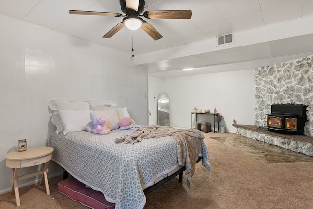 bedroom featuring ceiling fan, a wood stove, and carpet floors