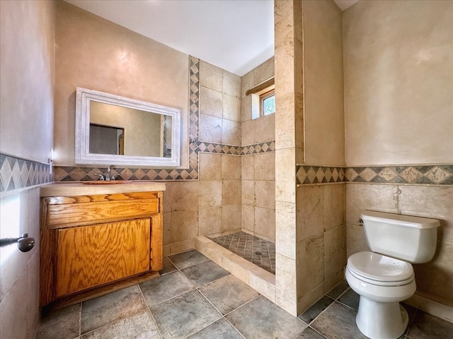 bathroom with vanity, toilet, a shower, and tile walls