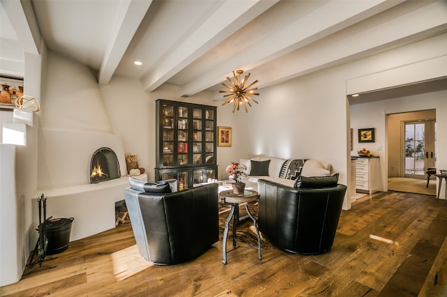 living room featuring beam ceiling, a large fireplace, wood-type flooring, and a notable chandelier