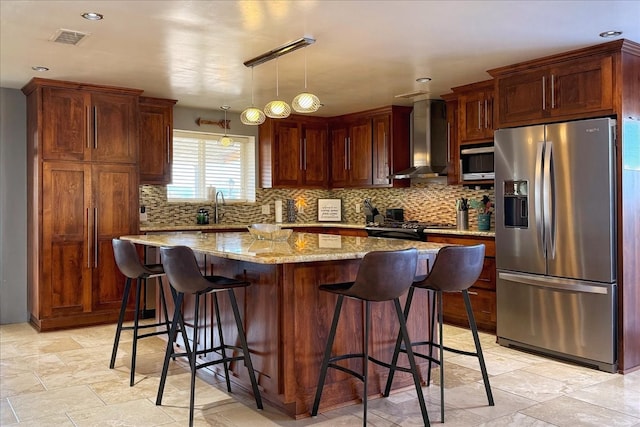 kitchen featuring a center island, wall chimney range hood, light stone counters, pendant lighting, and appliances with stainless steel finishes