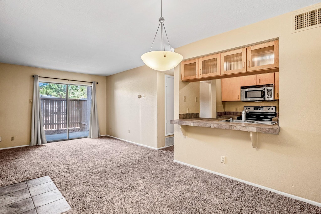 941 Calle Mejia Unit 630, Santa Fe, NM 87501 - kitchen featuring stainless steel appliances, glass insert cabinets, carpet floors, a kitchen breakfast bar, and pendant lighting