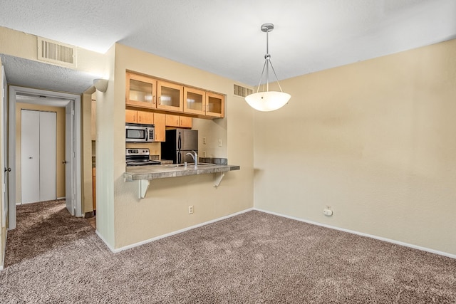 kitchen with pendant lighting, stainless steel appliances, dark carpet, and a breakfast bar area