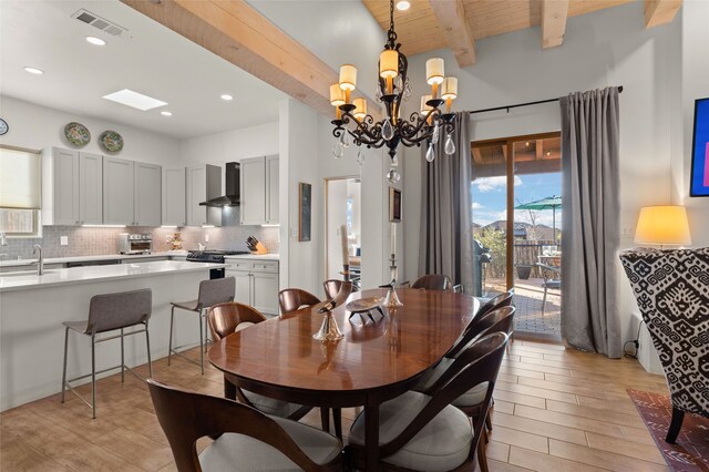 dining area with light wood finished floors, a toaster, visible vents, beamed ceiling, and a notable chandelier