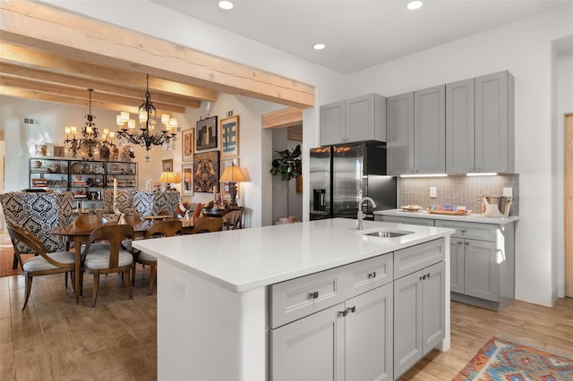 kitchen featuring beam ceiling, sink, stainless steel fridge, a center island with sink, and light wood-type flooring