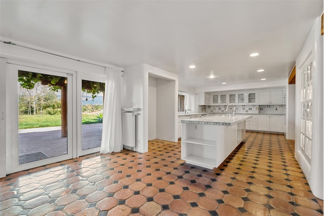 kitchen with backsplash, sink, white cabinets, and a kitchen island