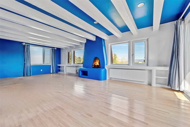 unfurnished living room featuring radiator, plenty of natural light, beamed ceiling, and light wood-type flooring