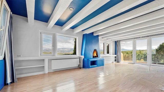 unfurnished living room with radiator heating unit, beamed ceiling, plenty of natural light, and light hardwood / wood-style flooring