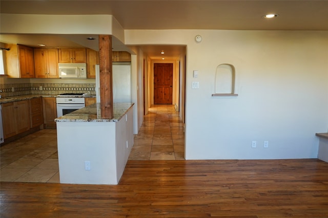 kitchen with decorative backsplash, white appliances, stone countertops, and light hardwood / wood-style flooring