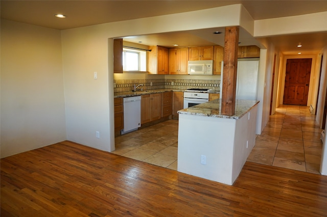 kitchen with stone countertops, a peninsula, white appliances, a sink, and light wood-style floors