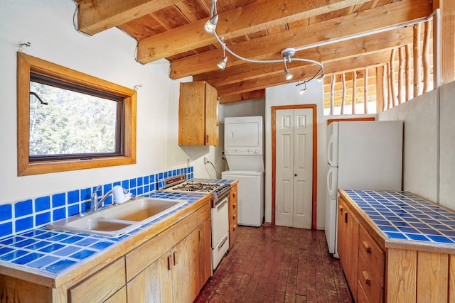 kitchen featuring tile countertops, white appliances, sink, stacked washer / drying machine, and beam ceiling