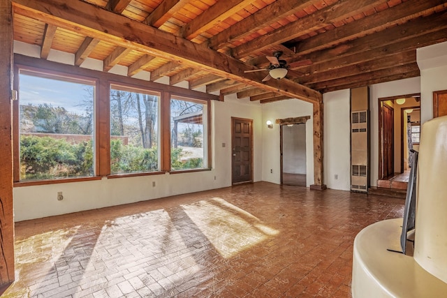 unfurnished sunroom featuring beamed ceiling, ceiling fan, wood ceiling, and a wealth of natural light