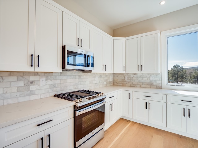 kitchen with stainless steel appliances, tasteful backsplash, light stone counters, light hardwood / wood-style flooring, and white cabinets