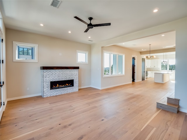 unfurnished living room with plenty of natural light, light hardwood / wood-style floors, a fireplace, and ceiling fan with notable chandelier