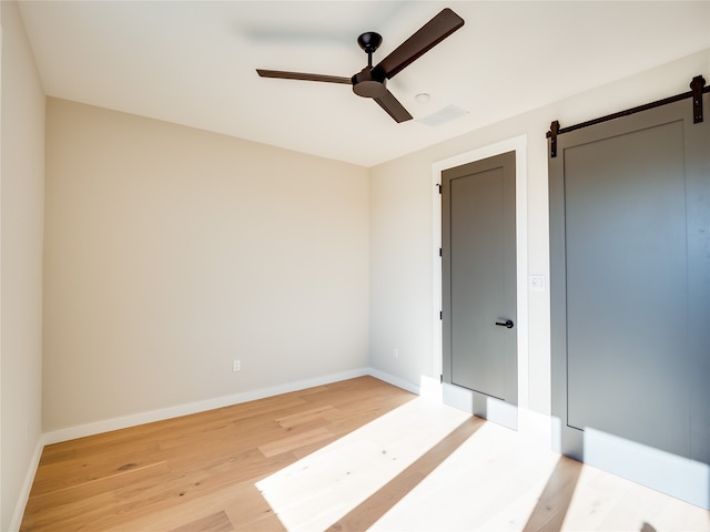 unfurnished room with ceiling fan, a barn door, and light hardwood / wood-style flooring