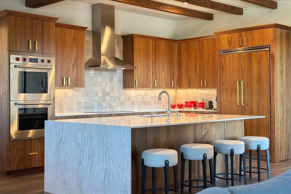 kitchen featuring a center island with sink, wall chimney range hood, sink, black electric cooktop, and stainless steel double oven