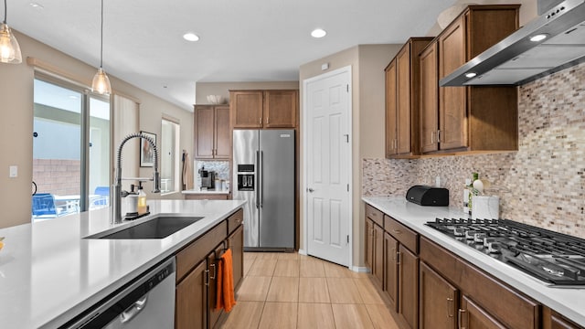 kitchen featuring a sink, appliances with stainless steel finishes, light countertops, and wall chimney range hood