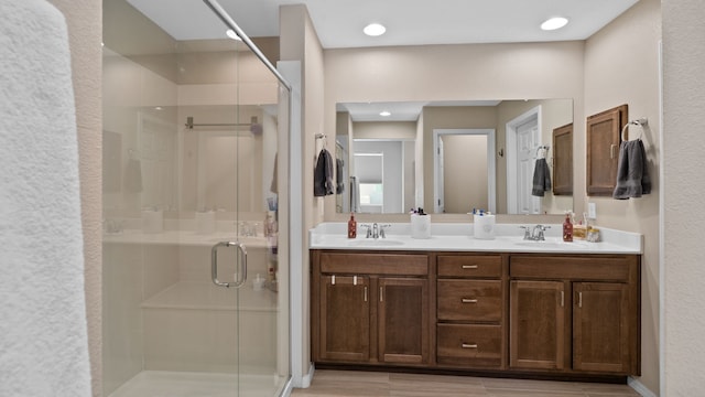 full bathroom with a shower stall, wood finished floors, double vanity, and a sink