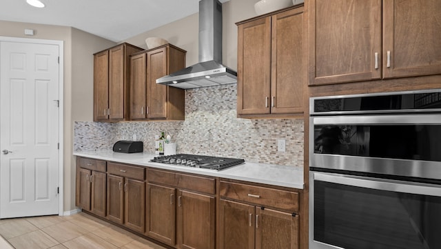 kitchen featuring appliances with stainless steel finishes, wall chimney exhaust hood, light countertops, light tile patterned floors, and decorative backsplash