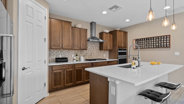 kitchen featuring visible vents, stainless steel appliances, a sink, wall chimney exhaust hood, and tasteful backsplash